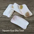 Strumento Gua Sha quadrato in conchiglia naturale con bordi lisci su legno scuro - Tavola Gua Sha di Conchiglia