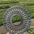 Rundes Evil Eye Wanddeko-Set aus Metall vor einem natürlichen grünen Feldhintergrund - Retro Silber Blaues Auge