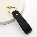 Detail of a black leather keychain with a gold heart pendant engraved with This Love - Black