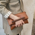 Braune Leder-Clutch-Tasche mit schwarzen Metallnieten, gehalten von einem Model im Anzug - Braun