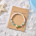 Sommerliches Strand-Perlenarmband mit Seestern-Anhänger auf Kraftpapier-Karte im Sand - Seestern Blau & Grün Perlen Stil (BR25Y0076)