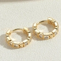 Dettaglio di orecchini placcati oro con zirconi chiari su sfondo beige testurizzato - ES2385-2 Orecchini in Zircone Bianco