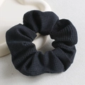 Dettaglio di scrunchie in velluto a coste nero con morbida consistenza su sfondo beige - Nero