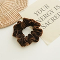 Scrunchie in velluto marrone scuro su superficie bianca con oggetti decorativi - Marrone