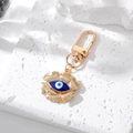 Golden flower keychain with blue evil eye charm and metal hook on white stone stand - Dark Blue Flower Eye