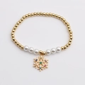 Detalle de pulsera dorada con perlas y un colgante de copo de nieve con gemas de colores - Colgante de Copo de Nieve