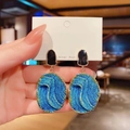Blue oval drop earrings with gold wave texture and silver posts in a handheld view - Wave Pattern Oval Earrings / Blue
