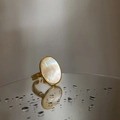 Detalle de anillo ovalado de nácar con banda dorada reflejado en una superficie de espejo mojado - JZ9198 Anillo de Madreperla Ovalado Dorado
