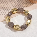 Detalle de cuentas irregulares de acrílico y esferas metálicas doradas en una pulsera - Gris