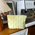 Pale yellow quilted makeup bag with textured pleats and metal zipper on wooden table - Yellow