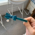 Detail of blue acetate bow hair clip with pearl pendant and golden logo engraving - Peacock Green Bow