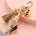 Gros plan du porte-clés coquillage avec clochette dorée et pompon en daim doux - Style Gland et Clochette en Coquillage