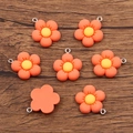 Orange resin flower charms with yellow center and metal loop on wooden surface - Orange