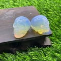 Pair of translucent blue crystal skull carvings with iridescent finish on wooden base - Opal