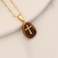 Macro view of golden cross pendant featuring a brown tiger eye stone on a chain - Tiger Eye
