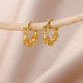 Close-up of gold chunky curb chain hoop earrings hanging on a natural wooden branch - Gold Cuban Link Texture Huggie