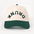 Close-up of 3D embroidered DRUNK text on a color-block baseball cap with contrast brim - Cream/Dark Green