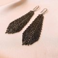 Dettaglio degli orecchini a foglia con nappe e strass neri su sfondo di tessuto beige morbido - Stile Piuma (HE10441) / Nero