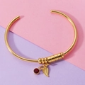Detalle de brazalete dorado abierto con circón rojo de nacimiento y dije de hoja - Piedra de Nacimiento de Octubre / Dorado