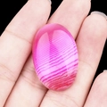 Pink striped agate oval cabochon stone for jewelry making held between fingers - Rose Red Agate