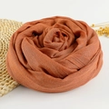 Solid reddish-brown linen cotton scarf rolled into a rose shape on a natural woven mat - 190x100cm / Rust Red