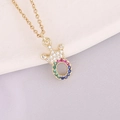 Detail of 18K gold necklace featuring a rainbow zircon crown pendant on a white plate - Letter O Style
