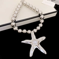 Gros plan d'un pendentif étoile de mer argenté avec chaîne à billes sur velours noir - Collier de Perles Étoile de Mer Argenté (72)