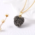 Vue détaillée d'un pendentif coeur doré serti de cristaux gris sur une céramique - Noir