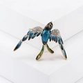 Dettaglio della spilla a uccello in smalto blu con strass lucidi su ali dorate - Serie Blu