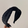 Close-up of black textured fabric headband with cross knot detail held by hand - Black
