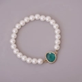 Detail of white glass pearl bracelet featuring a green gemstone pendant with gold trim - Malachite green