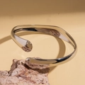 Makro-Detail des gedrehten silbernen Metallarmbands mit polierter Spiegeloberfläche - Silber