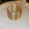 Macro-opname van een gouden meerlaagse brede armband op een wit keramieken bord - Eco Goud