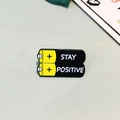 Battery shaped enamel pin with yellow and black colors featuring Stay Positive text - Stay Positive Battery