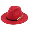 Detailed macro view of the gold leaf metal accent and black band on the red wool jazz hat - Red