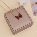 Detailansicht einer goldenen Kette mit braunem Bernstein-Schmetterling-Glasanhänger auf Box - Kaffeebraun
