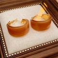 Detail view of gold C-shaped earrings with amber resin on a beige linen display pad - Amber Brown
