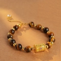 Detailed shot of tiger eye stone bracelet with golden hollow cylinder and red gemstone - Character Cylinder Tiger Eye Bracelet (Exquisite Gift Box)
