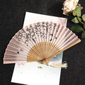 Pink silk folding fan with black flowers, bamboo ribs, and a beige tassel accessory - Cherry Blossoms Falling - Wood Color Handle