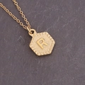 Macro shot of a golden hexagonal pendant with an embossed letter R on stone background - Letter R (18#R)