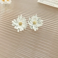 Close-up of daisy stud earrings with white petals and yellow centers on a striped surface - White