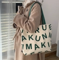 Minimalist beige canvas tote bag with large green lettering and green shoulder strap - KUNM Green Letters