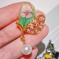 Dettaglio di spilla a farfalla dorata con fiori secchi rosa e una perla bianca appesa - Stile Farfalla Perla Rosa