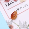 Macro detail of striped orange agate teardrop pendant on a floral decorative card - Red Agate