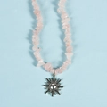 Pink irregular crystal chip necklace with a silver sun pendant on a light blue surface - Rose Quartz Sun