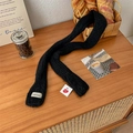 Slim black knitted skinny scarf with VEGETABLE label on rustic wooden surface - Black
