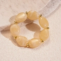 Vista de cerca de pulsera de cuentas acrílicas crema con detalles dorados sobre piedra - Marrón