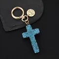 Detailed close-up of a golden cross keychain with blue rhinestones on a textured base - Blue