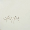 Detailed view of silver bow earrings with a textured finish on a neutral background - Short Style / Silver