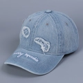 Dettaglio del cappellino in denim lavato con toppe sfrangiate e ricami in corsivo - Azzurro